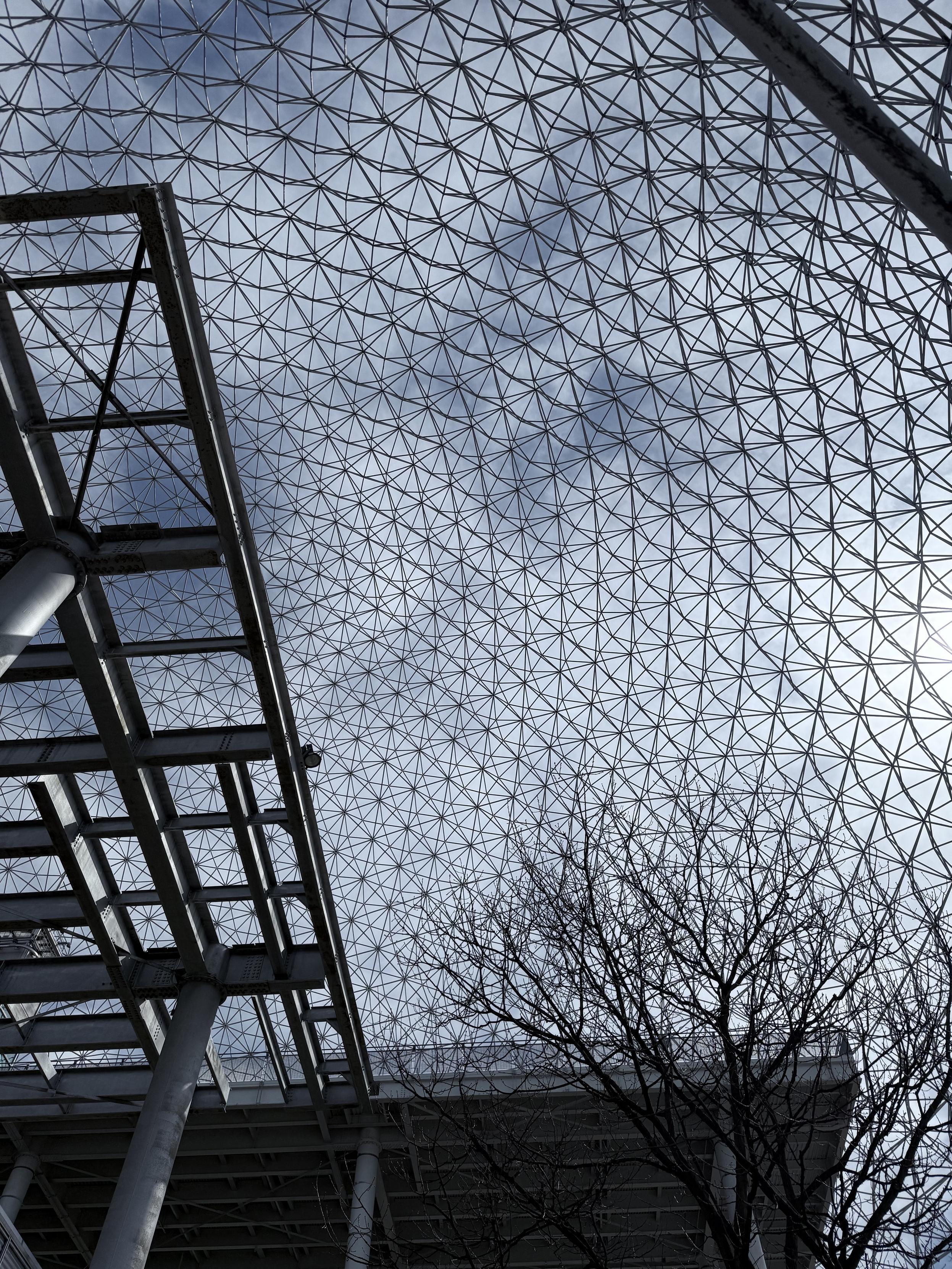 The Montreal Biosphere, seen from the inside. There's a metallic structure on the left and the iconic sphere structure on the right side, but it's looking upward, towards the sky.