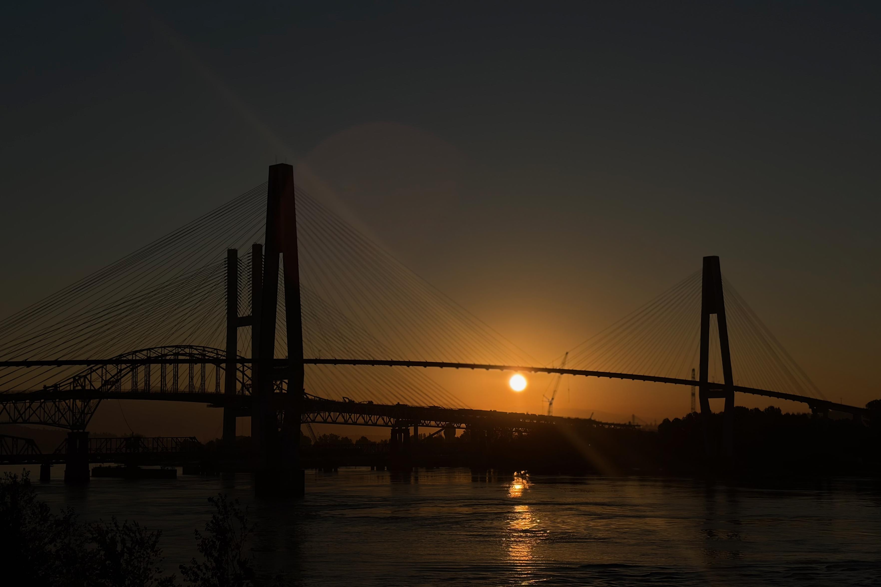 A silhouette of 4 bridges with a rising sun behind it, casting a warm glow over the water below.