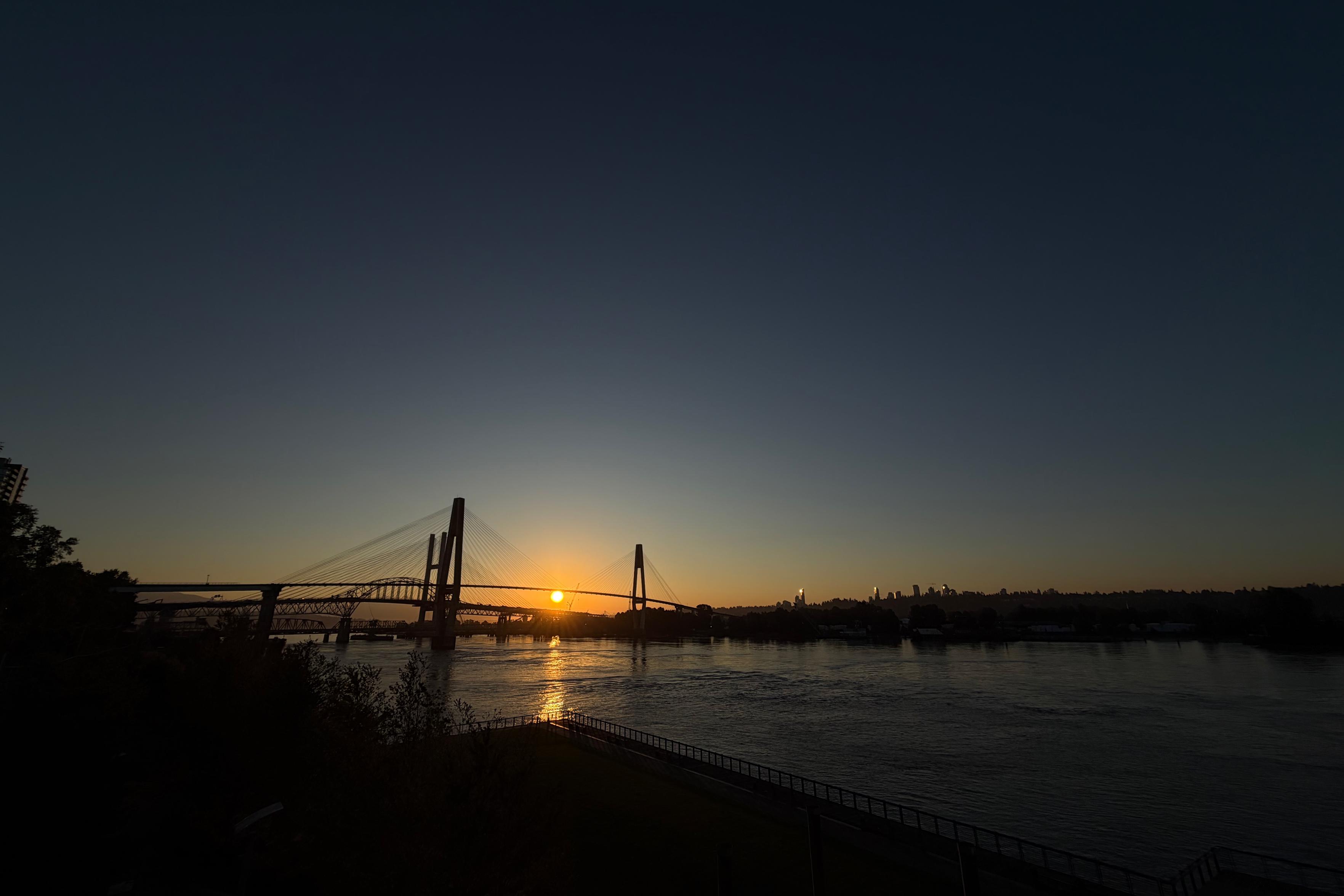 A silhouette of 4 bridges with a rising sun behind it, casting a warm glow over the water below.