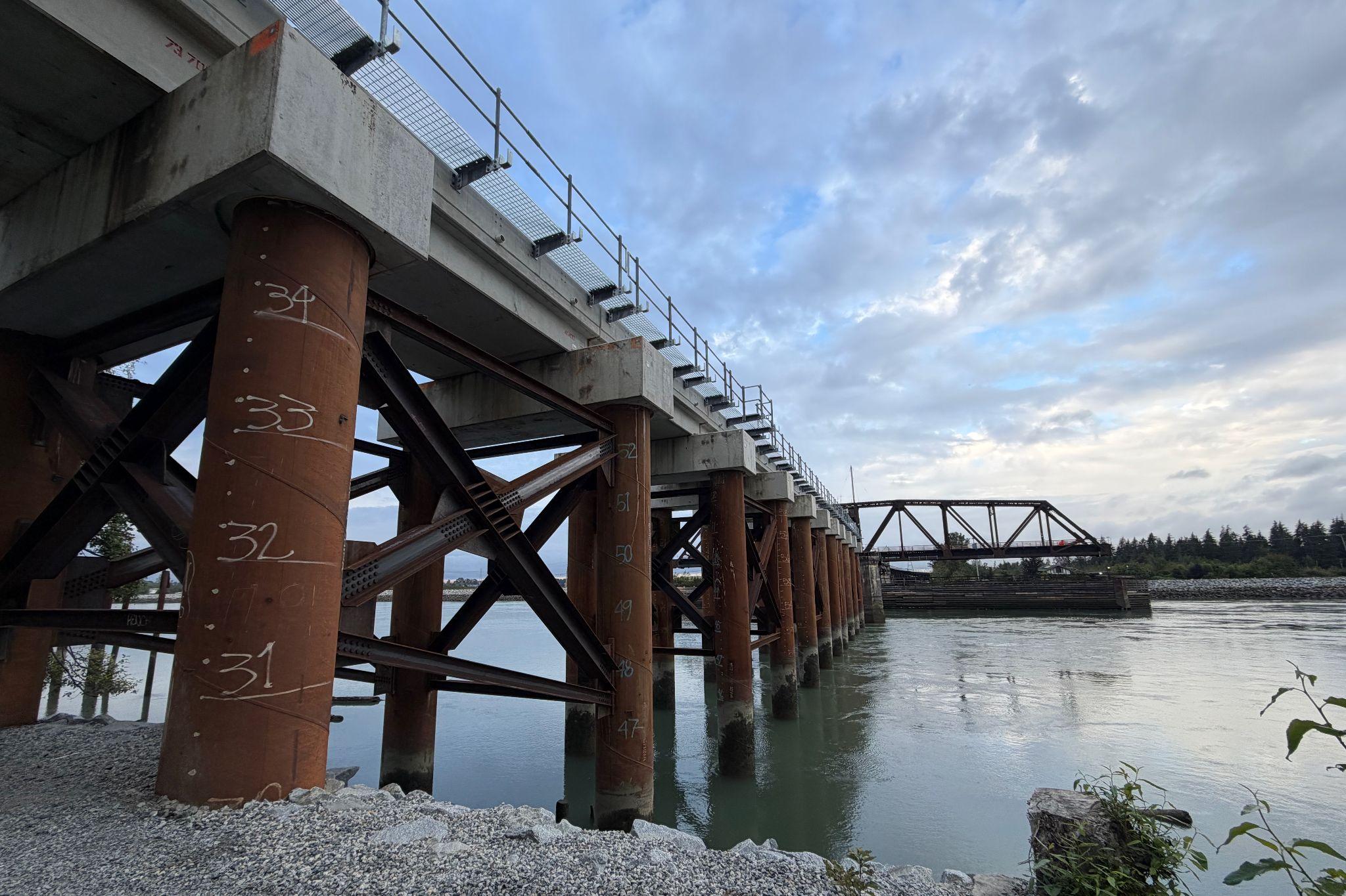 A bridge with brown pillars and white numbers written on them, spanning a body of water with a cloudy sky above.